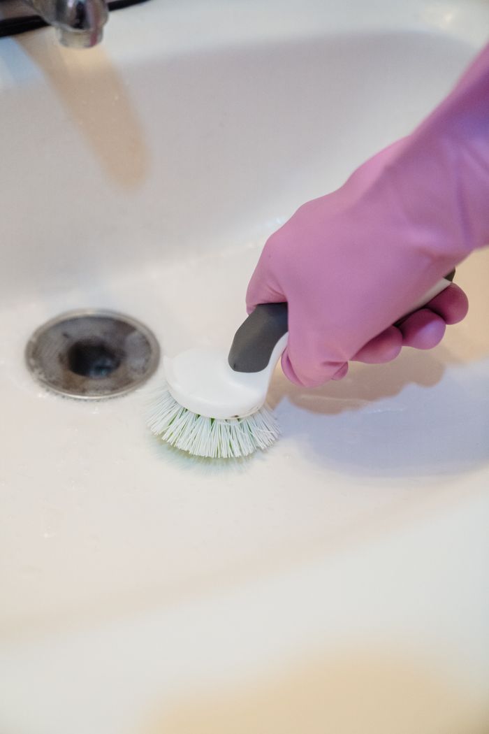 A close-up shot of a gloved hand scrubbing a sink with a scrub brush.